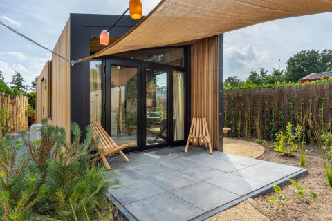 Casa tiny moderna en Holiday Park De IJsvogel, Países Bajos, con patio, fachada de madera y dos sillas.
