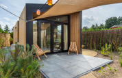 Casa tiny moderna en Holiday Park De IJsvogel, Países Bajos, con patio, fachada de madera y dos sillas.