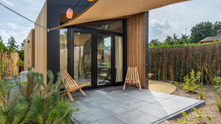 Casa tiny moderna en Holiday Park De IJsvogel, Países Bajos, con patio, fachada de madera y dos sillas.