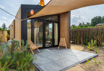 Casa tiny moderna en Holiday Park De IJsvogel, Países Bajos, con patio, fachada de madera y dos sillas.