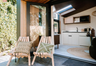 View inside Tiny Wellness Cabin at Holiday Park De IJsvogel, showing cozy outdoor chairs and modern kitchen.