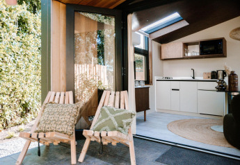 Intérieur de la Tiny Wellness Cabin au Holiday Park De IJsvogel avec chaises extérieures et cuisine moderne.