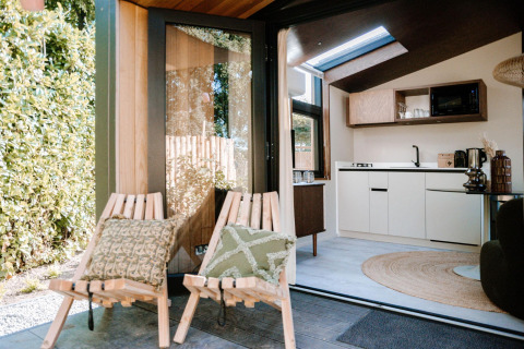 Vista de la Tiny Wellness Cabin en Holiday Park De IJsvogel con sillas al aire libre y cocina moderna.
