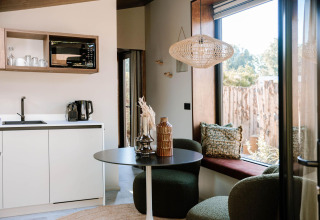 Interno moderno con angolo cottura, tavolo da pranzo e grande finestra nella Tiny Wellness Cabin, Holiday Park De IJsvogel.