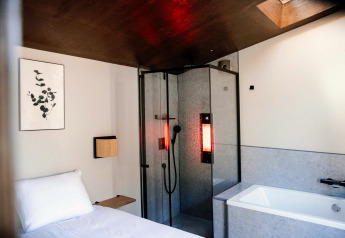 Cozy tiny wellness cabin with bed, shower featuring red light, and bathtub at Holiday Park De IJsvogel.