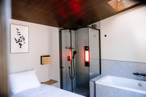 Cozy tiny wellness cabin with bed, shower featuring red light, and bathtub at Holiday Park De IJsvogel.