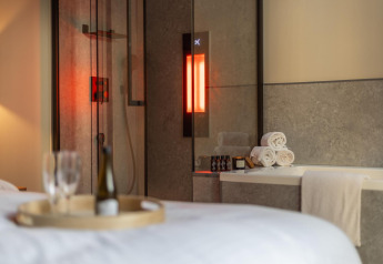 Bagno wellness nella Tiny Wellness Cabin di Holiday Park De IJsvogel con luci soffuse, asciugamani e vino.