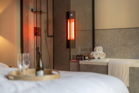 Bagno wellness nella Tiny Wellness Cabin di Holiday Park De IJsvogel con luci soffuse, asciugamani e vino.