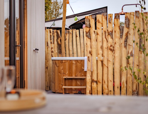 Bañera de hidromasaje de madera al aire libre junto a una valla rústica en Tiny Wellness Cabin, Holiday Park De IJsvogel, Países Bajos.