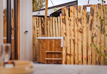 Vasca da bagno in legno all'aperto e recinzione rustica alla Tiny Wellness Cabin presso Holiday Park De IJsvogel, Paesi Bassi.