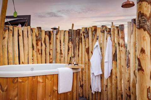 Zona de bienestar al aire libre con bañera, batas y ducha en la Tiny Wellness Cabin de De IJsvogel, Países Bajos.