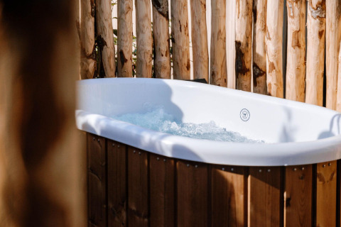 Bañera exterior con agua burbujeante en Tiny Wellness Cabin, Holiday Park De IJsvogel, Países Bajos, rodeada de madera.