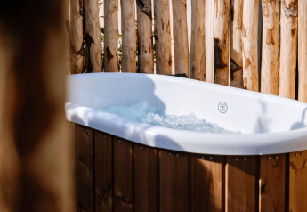 Bañera exterior con agua burbujeante en Tiny Wellness Cabin, Holiday Park De IJsvogel, Países Bajos, rodeada de madera.