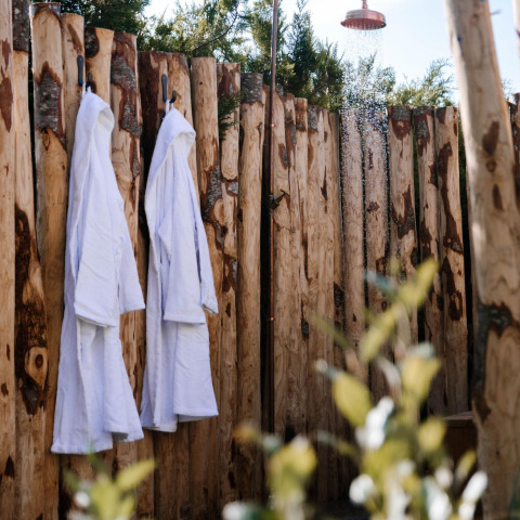 Ducha exterior y dos albornoces blancos colgados en una valla de madera rústica en Tiny Wellness Cabin, Países Bajos.
