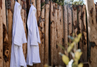 Doccia esterna e due accappatoi bianchi appesi a una recinzione in legno al Tiny Wellness Cabin nei Paesi Bassi.