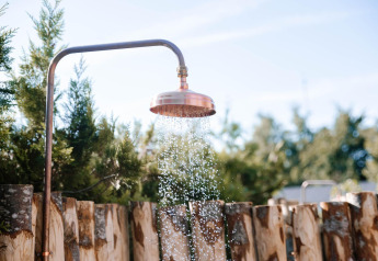 Outdoor shower with copper showerhead at Tiny Wellness Cabin, De IJsvogel, Netherlands, surrounded by trees.