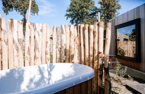 Outdoor bathtub with a wooden fence at Tiny Wellness Cabin, Holiday Park De IJsvogel, Netherlands, on a sunny day.