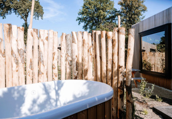 Bañera exterior junto a una valla de madera en Tiny Wellness Cabin, Holiday Park De IJsvogel, Países Bajos, en un día soleado.