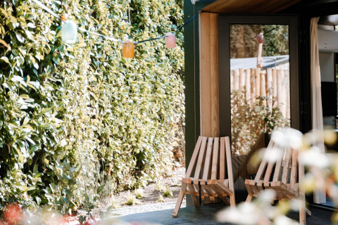 Außenbereich der Tiny Wellness Cabin im Holiday Park De IJsvogel mit Holzstühlen und grüner Hecke.