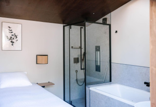 Modern tiny wellness cabin with bed, shower and bathtub at Holiday Park De IJsvogel in the Netherlands.
