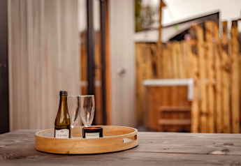 Et træbord med en bakke med en vinflaske, to glas og et lys i Tiny Wellness Cabin, De IJsvogel, Holland.