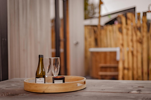 Houten tafel met een dienblad met wijnfles, twee glazen en een kaars in Tiny Wellness Cabin, De IJsvogel.