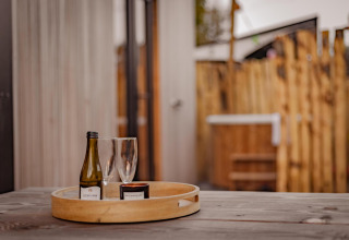 Houten tafel met een dienblad met wijnfles, twee glazen en een kaars in Tiny Wellness Cabin, De IJsvogel.