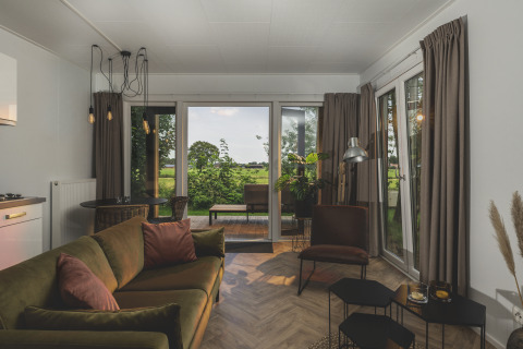 Gezellige woonkamer in River Lodge Wellness bij Holiday Park Mölke, Nederland, met zicht op velden buiten.