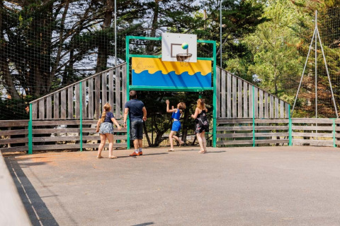 Family enjoys a game of basketball outdoors at Camping Le Bois de la Gachère holiday park in France.