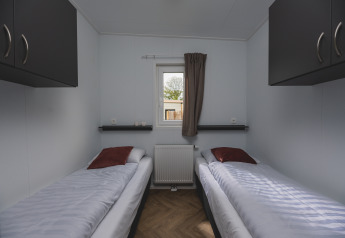 Twee enkele bedden in een lichte kleine kamer van Panorama Lodge in Vakantiepark Hölte, Nederland.