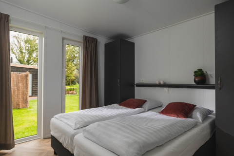 Dormitorio luminoso en Panorama Lodge con dos camas individuales y vista al jardín en Vakantiepark Hölte, Países Bajos.