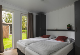 Lichte slaapkamer in Panorama Lodge met twee eenpersoonsbedden en tuinzicht, Vakantiepark Hölte, Nederland.