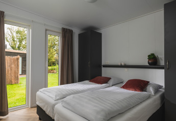 Lichte slaapkamer in Panorama Lodge met twee aparte bedden en zicht op tuin, Vakantiepark Hölte, Nederland.