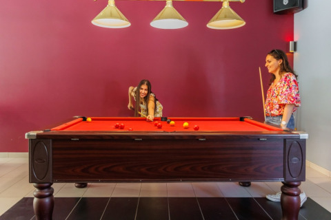 Two women playing pool at a billiard table in Camping Le Bois de la Gachère holiday park in France.