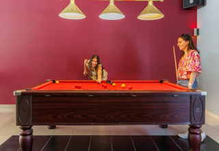 Two women playing pool at a billiard table in Camping Le Bois de la Gachère holiday park in France.
