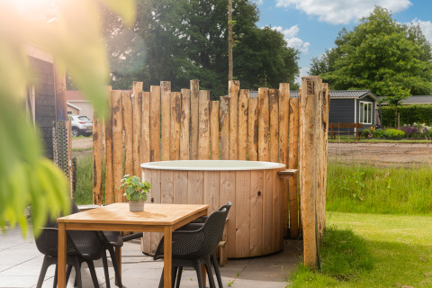 Outdoor wooden hot tub and dining table at Panorama Lodge, Vakantiepark Hölte, Netherlands in sunlight.