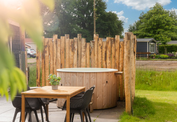 Outdoor wooden hot tub and dining table at Panorama Lodge, Vakantiepark Hölte, Netherlands in sunlight.