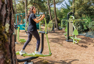 Frau trainiert an Outdoor-Fitnessgeräten in einem bewaldeten Ferienpark in Pays de la Loire, Frankreich.