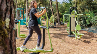Kvinde træner på udendørs fitnessudstyr i en skovklædt feriepark i Pays de la Loire, Frankrig.