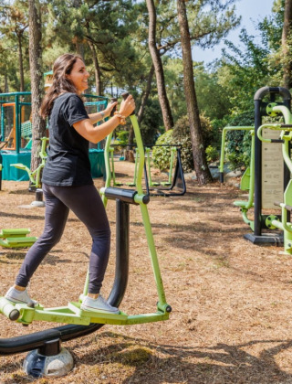 Kvinde træner på udendørs fitnessudstyr i en skovklædt feriepark i Pays de la Loire, Frankrig.