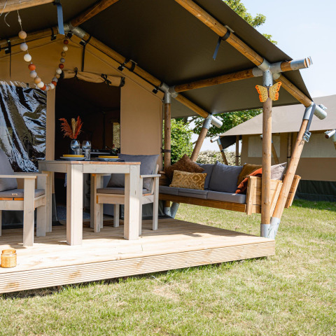 Safari-Zelt Cozy mit Frühstück bei TinyParks Cast Away in den Niederlanden, mit Holzveranda und Sitzbereich.