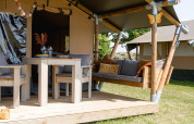 Tenda safari Cozy con colazione presso TinyParks Cast Away nei Paesi Bassi, veranda in legno e area salotto.