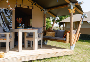 Safari tent Cozy with breakfast at TinyParks Cast Away in the Netherlands, featuring a wooden porch and seating.