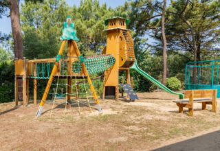 Spielplatz mit Klettergerüst, Rutsche und Holzbänken im Camping Le Bois de la Gachère in Pays de la Loire.