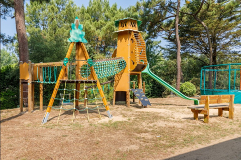 Parque infantil con estructura para trepar, tobogán y bancos de madera en Camping Le Bois de la Gachère.