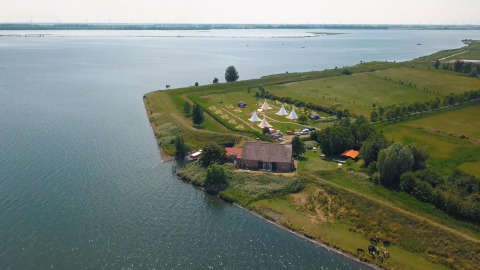 Vista aérea de la tienda Safari Cozy en TinyParks Cast Away, Países Bajos, junto a un lago y campos verdes.