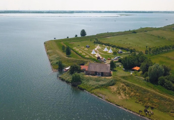 Vista aerea della tenda Safari Cozy presso TinyParks Cast Away nei Paesi Bassi, tra lago e campi verdi.