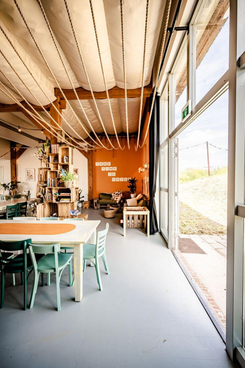 Interior of a safari tent with a cozy lounge, dining table, bookshelves, and bright natural light in the Netherlands.