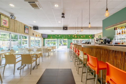 Zona pranzo luminosa e moderna con bar e sedie colorate al Camping Le Bois de la Gachère in Francia.