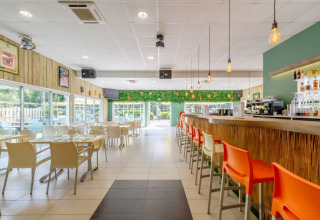 Espace de restauration lumineux et moderne avec bar et chaises colorées au Camping Le Bois de la Gachère, France.